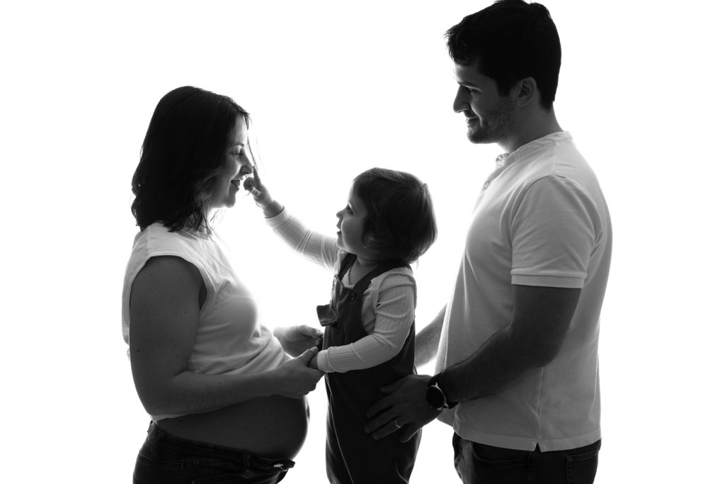 Portrait de famille en jeans et tee shirt blanc, le couple et leur enfant posant pour une séance grossesse en Moselle