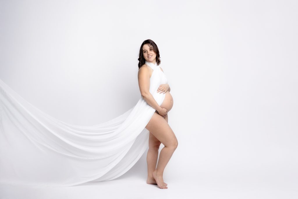 Future maman en voile blanc posant en studio lors d’une séance photo maternité à Florange en Moselle.