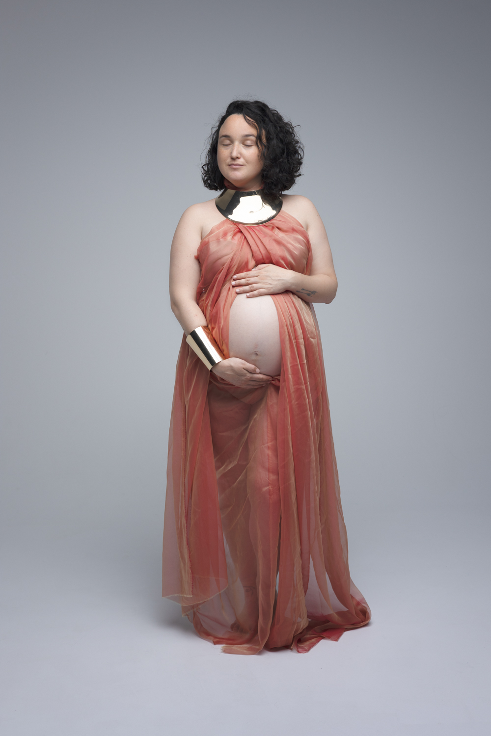 Future maman en robe orange en voile posant lors d’une séance photo maternité à Florange en Moselle.