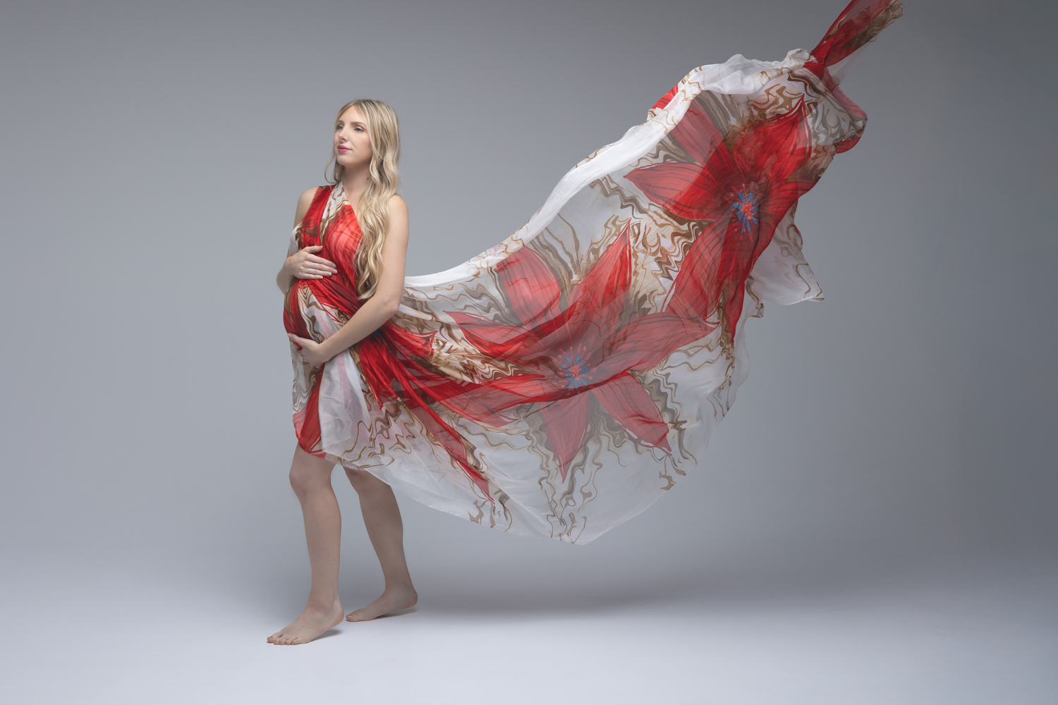 Future maman en voile avec un motif fleur qui vole dans les airs posant en studio lors d’une séance photo maternité à Florange en Moselle.