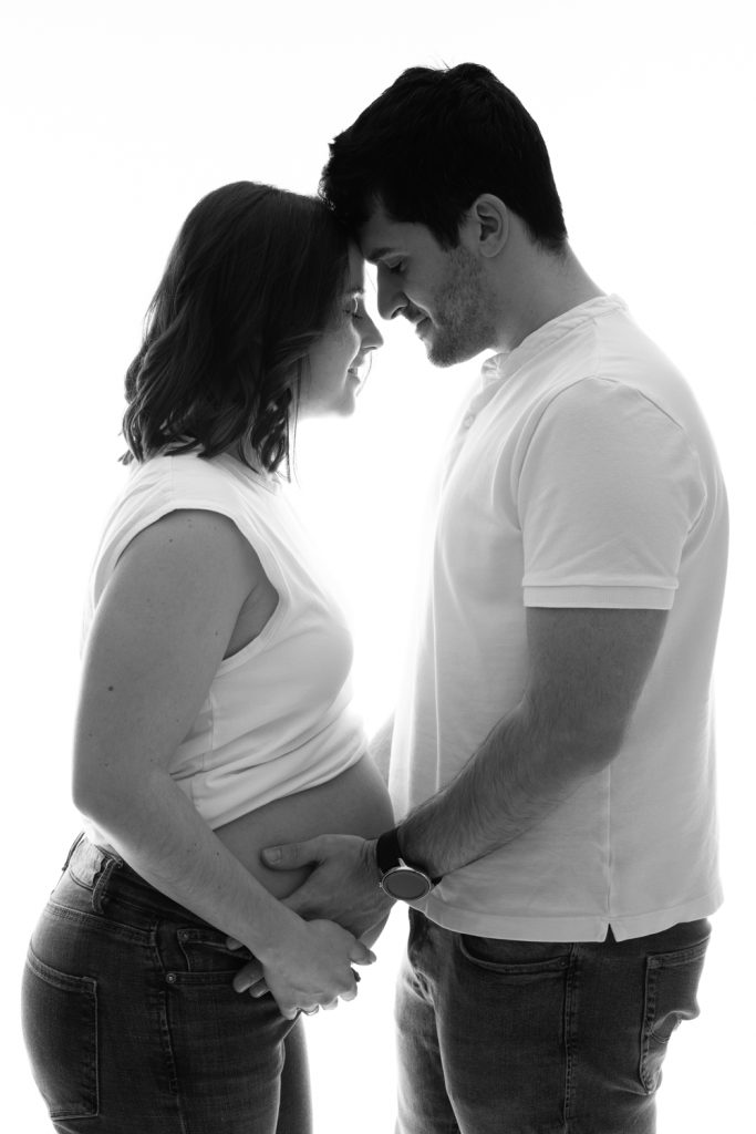 Couple en jeans attendant un enfant lors d’une séance grossesse en studio.