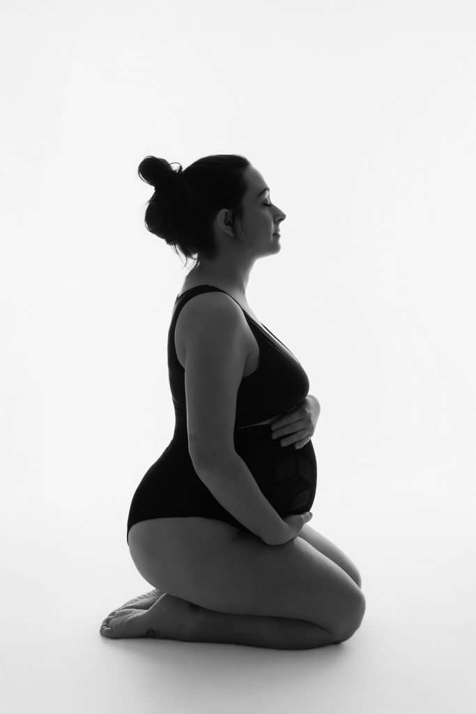 Femme enceinte sur genoux au sol pour un shooting grossesse en noir et blanc