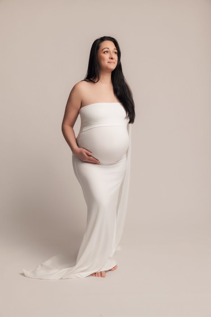 Femme enceinte en studio photo en robe blanche